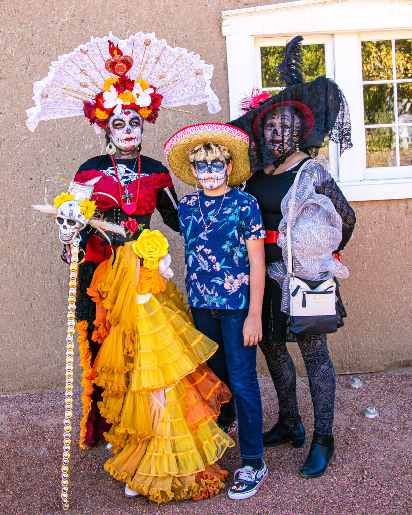 Three people adorned in regalia in celebration in Day of the Dead.